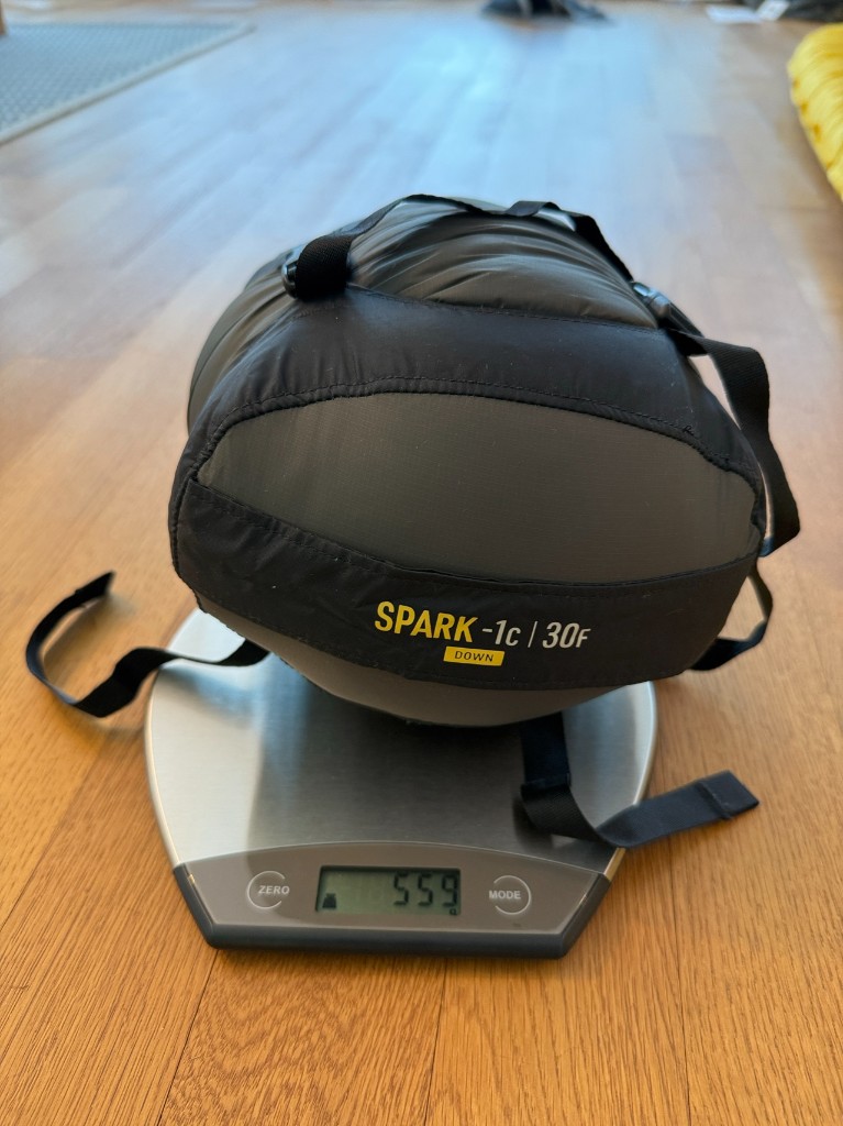 Sea to Summit Spark -1 in its black compression stuff sack on a digital kitchen scale reading 559 grams.